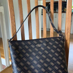 Guessväska - Snygg guess väska i brunt, använd några gånger vilket syns på sista bilden då det finns spår av smink fläckar inuti väskan, förutom det är den i väldigt bra skick