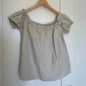 Beige offshoulder topp Vero Moda - Supersöt beige offshoulder topp från Vero Moda med korta puffärmar och resår vid halsringningen. Tillverkad i mjuk bomull, perfekt för varma dagar. Enkel och stilren design som är lätt att matcha med dina favoritjeans eller kjol.