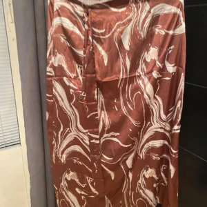 Glansig beige skjorta med rynkade detaljer - Snygg beige skjorta från amish i glansigt material med v-ringning och rynkade detaljer framtill. Skjortan har långa ärmar med breda manschetter och knappar framtill. Perfekt för dig som vill ha en trendig och stilren look.