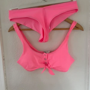 Rosa bikini från Censored, strl M - Supersnygg bikini i rosa färg från Censored. Toppen har ribbad struktur, knappar framtill och en söt knytning under bysten. Bikinitrosan är enkel med lite scrunch på baksidan. Perfekt för stranden eller poolen i sommar! Aldrig använd men är nytvättad. Läs gärna bio💕