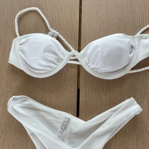 Vit bikini med tvinnade axelband - Snygg vit bikini med vadderad bygel-bh och tvinnade axelband. Underdelen är enkel och stilren med en klassisk passform. Perfekt för stranden eller poolen, ger en fräsch och clean look.