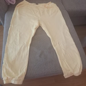 Gula mjukisbyxor med resår - Snygga ljusgula mjukisbyxor med resår i midjan och vid bensluten. Byxorna är i mjukt bomullstyg och har en avslappnad passform, perfekta för chill dagar hemma eller när du vill vara bekväm. Enkla att matcha med en t-shirt eller hoodie. Byxor had "s" storlek tshirt har "M" storlek. Jag har en annan st som båda är L storlek. 