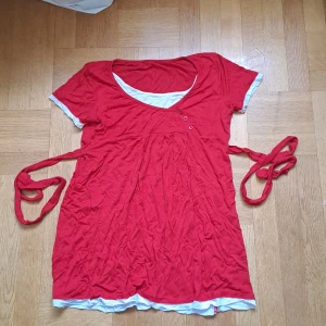 Röd topp med knytband - Superfin röd topp med insydd lager på lager i vitt. Toppen har korta ärmar, knytband i midjan och tre små knappar framtill. Pris är diskuterbart vid snabb affär! 🩷😊 uppskattad storlek S-M. Har legat i garderob. 