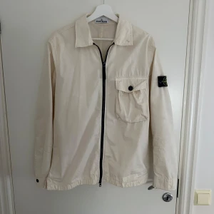 Beige overshirt från Stone Island - Säljer en snygg beige overshirt från Stone Island. Perfekt för vår och höst! Den har en bröstficka med knapp och är i mycket bra skick. Storlek M