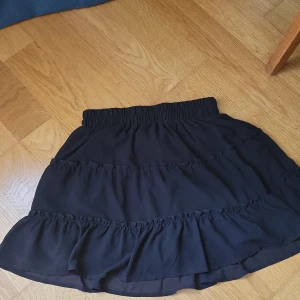 Svart volangkjol från Sisters Point - Supersöt svart kortkjol från New yorker  med flera volanglager och bred resår i midjan. Kjolen är luftig och har en flowy känsla, perfekt till sneakers eller boots. Enkel att matcha och ger en chill men ändå stylish vibe.