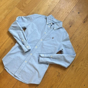 Ralph Lauren skjorta (pris diskuterbart) - !! NY SKICK !!Snygg ljusblå skjorta från Ralph Lauren i SLIMFIT storlek 20 sitter som en S-M med klassisk button-down krage och broderad logga på bröstet. Skjortan har lång ärm, normal passform och är tillverkad i mjuk bomull. Perfekt till jeans för en clean och stilren look.