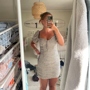 Prickig kort klänning från Zara - Supersöt kort klänning från Zara i beige med svarta prickar. Klänningen har puffiga korta ärmar, smockad passform och söt knytning framtill. Obs det lilla hålet vid sömmen. Jag har inte dragit upp dragkedjan, pga klänningen är för tajt på mig. Dragkedjan är som ny. Hålet går lätt att laga med några stygn.