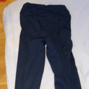 Svarta träningstights med reflexdetalj - Säljer ett par svarta tights perfekta för träning. De har hög midja, praktiska sidfickor och en snygg reflexdetalj vid vristen. Materialet är stretchigt och följsamt, vilket gör dem riktigt bekväma. Passformen är tight och de sitter på plats under hela passet.