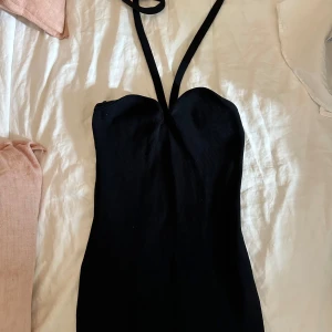 Svart axelbandslös ribbad klänning från Zara midi  - Snygg svart kortklänning från Zara med smala halterneckband. Klänningen är figurnära och har en enkel, stilren design som passar perfekt när du vill känna dig extra chic. Materialet är mjukt och följsamt.