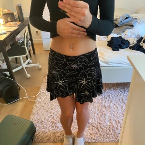 Svart blommig strandkjol från Ossian - Supersöt svart strandkjol från Ossian med vita blommor och asymmetrisk, vågig nederkant. Kjolen har en skön passform och är perfekt för dig som gillar en lite edgy och lekfull stil. Tunn och lätt, passar perfekt till varmare dagar. Det står att den är i storlek L men den är super stretchig. Passar mig som har storlek S i vanliga fall.