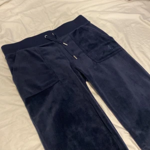 Mörkblå mjukisbyxor i velour - Mörkblå mjukisbyxor i mjuk velour med bred resår i midjan och snörning. Stora fickor fram och en bakficka med knappar. Perfekta för chill dagar och riktigt sköna att ha på sig. De är från juicy couture. De är i storlek S. Lite smutsiga är de men inget som inte går bort i tvätten. Säljer pga ingen användning. Lite nedtrampade i botten men annars ser de väldigt bra ut, inga hål. 