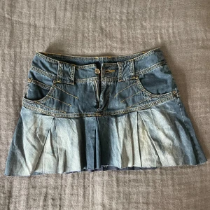 Lågmidjad volang jeanskjol - Snygg kort jeanskjol i mörkblått med volang och lågmidja. Kjolen är vintage och finns inte att köpa längre. Den har en cool och sliten nedre kant och sitter jätte skönt. Väldigt populär så köp snabbt, först till kvarn!