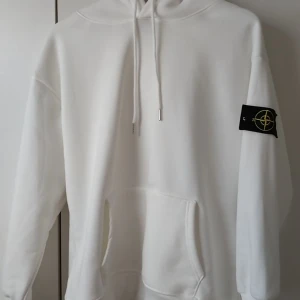 Vit hoodie från Stone Island - Säljer en clean vit hoodie från Stone Island med klassisk patch på ärmen och stor känguruficka framtill. Tröjan har huva med snörning och är tillverkad i mjuk bomull. Perfekt för dig som gillar stilrena streetwear-plagg. Kan MÖTAS i Malmö Trelleborg eller nära där 