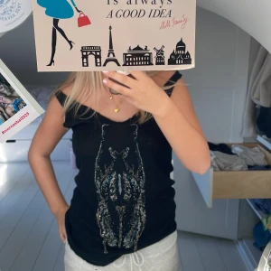 Svart linnetopp Zadig & Voltaire Deluxe - Svart linnetopp från Zadig & Voltaire Deluxe med snyggt mönster av små pärlor och paljetter framtill i silver och blått. Toppen är ärmlös med v-ringning och har en cool, lite rockig vibe. Perfekt att styla med jeans eller kjol för en edgy look.