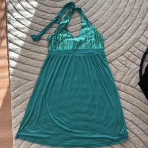 Turkos paljettklänning från H&M - Snygg turkos långklänning från H&M med glittriga paljetter upptill och djup v-ringning. Klänningen har smala axelband, knyt i nacken och ett flowy tyg i kjolen. Perfekt för dig som vill sticka ut med färg och glitter!