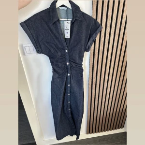 Mörkblå jeansklänning från Zara - Snygg långklänning i mörkblå denim från Zara med markerad midja, korta ärmar och knappar hela vägen framtill. Klänningen har en snygg slits nertill. Aldrig använt 
