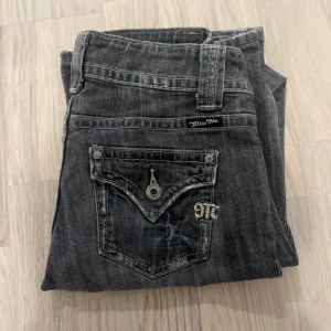 Grå Miss Me jeans med broderade fickor - Snygga grå jeans från Miss Me med slitna detaljer och broderade bakfickor med knappar och metallogo. Jeansen har raka ben och dubbla knappar i midjan. Perfekta för dig som gillar en cool och avslappnad stil. Längd: 102cm Midja: 36-38cm (stretch) benöppning: 24cm inseam: 81cm
