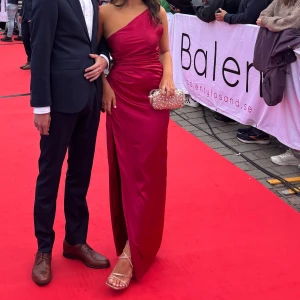 Vinröd långklänning med slits baby boo - Säljer en vinröd långklänning i glansigt material med oneshoulder och snygg slits framtill. Klänningen har figurnära passform och markerad midja, perfekt för bal eller student. Tyget har en lyxig satinlook och färgen är riktigt djup och elegant.     Balklänningen har bara blivit använd en gång och har fått två små mörkare cirklar på klänningen som verkligen inte syns ifall man inte kollar på extremt nära håll 