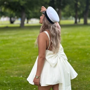 Vit kort klänning med stor rosett - Säljer min superfina student klänning med en stor rosett i ryggen. Köpt från Babyboo och använt endast en gång. Storlek M men då storlekarna är små så kan den även passa S. Har även både tvättat den hemma och kemtvättat den. 