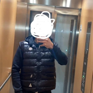 Svart dunväst från Moncler - Stilren Moncler-väst i toppskick! Perfekt för både vardag och exklusiva tillfällen. Ikonisk design, lättviktig men värmande – idealisk året runt. Passar dig som vill kombinera lyx med funktion. Begränsat antal – först till kvarn! Säkra din Moncler-väst idag och höj din stilnivå direkt!