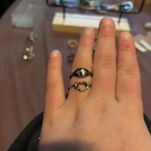 Två silverringar med yin yang och hjärta - Säljer två snygga silverfärgade ringar. Ena ringen har en svartvit yin yang-symbol i mitten och den andra är en tunn ring med ett öppet hjärta framtill. Perfekta att bära tillsammans eller var för sig för en cool och personlig stil.