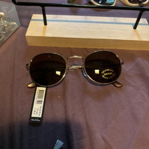 Ovala solglasögon från Montini - Snygga ovala solglasögon från Montini med tunna, silvriga metallbågar och bruna glas. Klassisk och stilren design som ger en cool vibe. Perfekta för att lyfta din look under soliga dagar.