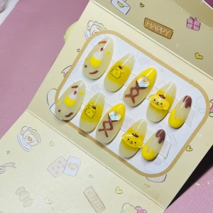 Söta Pompompurin lösnaglar gul/brun - Set med lösnaglar i mandelform med Pompompurin-motiv. Naglarna är i olika nyanser av gult och brunt, vissa med 3D-detaljer och hjärtformad dekoration. Perfekt för dig som älskar kawaii och vill ha unika naglar med söt design.