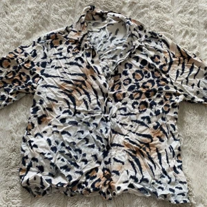 Leopardmönstrad skjorta i bomull - Snygg skjorta med leopardmönster i beige, svart och bruna toner. Skjortan har klassisk krage, knäppning framtill och långa ärmar. Tillverkad i mjuk bomull, perfekt för dig som vill sticka ut med ett djurmönster.