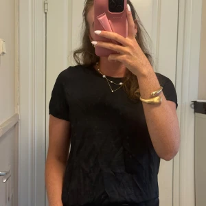 Svart t-shirt med spetsdetalj från Vila - Svart t-shirt från Vila i satinliknande material med rund hals och korta ärmar. Baksidan har en snygg spetsdetalj som ger en extra touch. Enkel och stilren modell som är lätt att matcha till olika outfits.