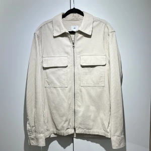 Beige manchesterjacka från H&M - Snygg beige manchesterjacka från H&M med raka linjer, två stora bröstfickor och dragkedja framtill. Jackan har klassisk krage och långa ärmar, perfekt för dig som gillar stilren och avslappnad look. XS men passar S-M