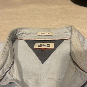 Ljusblå skjorta från Hilfiger Denim  - Snygg ljusblå skjorta från Hilfiger Denim i regular fit. Skjortan har klassisk krage, knäppning framtill och diskret logga broderad på bröstet. Tillverkad i mjuk bomull och har långa ärmar med knappar vid manschetterna. Perfekt för en clean och stilren look.