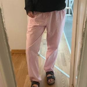 Rosa randiga mjukisbyxor med snörning - Säljer ett par chill rosa mjukisbyxor med vita tunna ränder. Byxorna har dragsko i midjan och raka, loose ben. Perfekta för softa dagar hemma eller när du vill vara bekväm men ändå se söt ut.