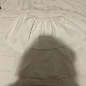 Vit axelbandslös volangtopp - Säljer min vita, trendiga volangtopp🌟Det kan finnas spår av smink högst upp längst kanten men det är inget som syns när den används. Om tröjan säljs så kommer jag såklart att försöka få bort de små spåren och jag tror att det är möjligt!