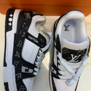 Louis Vuitton sneakers  - Snygga Louis Vuitton sneakers i svart och vitt med klassiskt LV-monogram och tydliga logodetaljer. Skorna har snörning, platt sula och är tillverkade i en mix av skinn och textil. Perfekta för dig som vill sticka ut med exklusiv streetstyle.