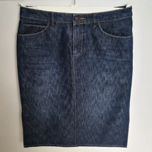 Mörkblå denim kjol från Esprit - Mörkblå denim kjol i rak modell med fem fickor, bälteshällor med slits i båda sidorna från Esprit. Kjolen stängs med knapp och dragkedja framtill. Kjolen är 63 cm lång, storlek 36. 