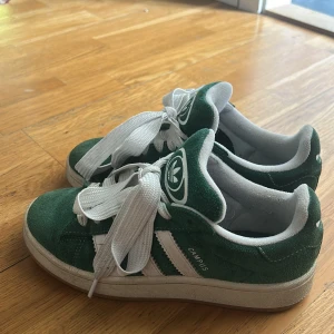 Adidas Campus gröna sneakers i mocka - Gröna Adidas Campus sneakers i mjuk mocka med vita detaljer och breda vita snören. Du får även med ett par tjocka gröna snören och ett par tunna gröna snören. Storlek 37 1/3