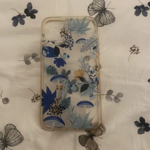 Blommigt mobilskal med blå detaljer - Snyggt mobilskal med transparent bas och blommigt mönster i blått, gult och grönt. Skalet har coola växt- och svampdetaljer som ger en unik vibe till din mobil. Perfekt för dig som vill ha något som sticker ut och känns personligt.