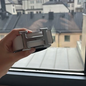 H bälte - Snyggt skärp från Herme-s i svart och vitt skinn med det ikoniska stora H-spännet i silver. Bältet har en stilren design med kontrasterande färger och exklusiv känsla. Perfekt accessoar för att lyfta din outfit med en lyxig touch.