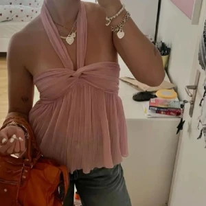 Plisserad rosa halterneck topp - Supersöt plisserad halterneck topp i ljusrosa med twistad detalj framtill. Toppen är ärmlös och har en flowy, luftig passform som ger en romantisk vibe. Perfekt för varma dagar och snygg att styla med både jeans och kjol.