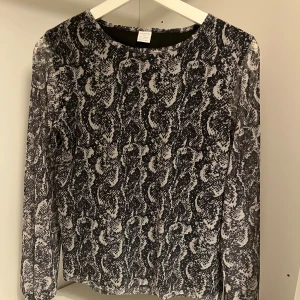 Svart meshblus med ormmönster Lindex - Snygg meshblus från Lindex i svart och grått med ormmönster. Blusen har lång ärm och är tillverkad i ett tunt, stretchigt material som känns lätt och luftigt. Perfekt för dig som vill sticka ut med ett coolt mönster.                                             Passar storlek s