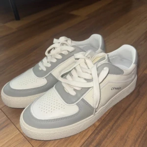 Vita och grå sneakers från Copenhagen - Snygga sneakers från Copenhagen i vitt och ljusgrått skinn. Klassisk modell med rund tå, perforerade detaljer och tjock vit sula. Skorna har snörning och stilren logga på sidan. Perfekta för en clean och trendig look. Funkar både på tjejer och killar. Hör av er vid frågor! Köpta för 1800kr säljer för 1000kr!