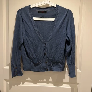 Blå kofta  - Snygg blå kofta från Zoul med v-ringning och knappar framtill. Koftan har två fickor och ribbade muddar vid ärmslut och nederkant. 