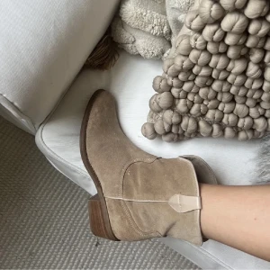 Beige mocka cowboy boots stl 38 - LÅNADE BILDER!! Snygga beige cowboy boots i mocka med låg klack och spetsig tå. Skorna har klassiska western-detaljer och en träfärgad sula. Perfekta för dig som vill ha söta skor under en sommarklänning. Skorna är jätte bekväma och passar mig som brukar ha 37,5 till 38. Skorna är köpte i Italien. 