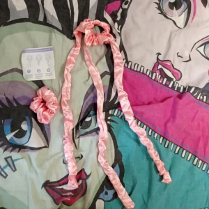 Rosa satin heatless curl med scrunchie - Snyggt rosa heatless curl i satin med matchande scrunchie, perfekt för att fixa håret utan tovor. Heatless curlen har långa, mjuka ben som flätas in i håret och ger en trendig look. Satinmaterialet är skonsamt mot håret och ger en lyxig känsla. 