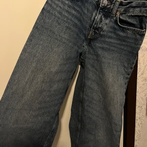 Blå raka jeans från H&M, strl 34 - Klassiska blå jeans från H&M i rak modell med hög midja. Jeansen har fem fickor, bälteshällor och stängs med knapp och dragkedja. Snygg tvättad denim som passar till allt. Materialet är 100% bomull för en autentisk jeanskänsla.