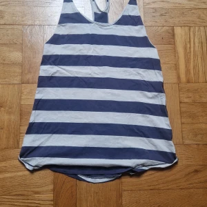 Randig linne från Lululemon - Blåvittrandigt långt linne från Lululemon, köpt i USA. Racerback, väldigt luftig och skön. En liten fläck på ryggen - se bild - kan gå bort med noggrannare tvättning, annars i fint skick. Lapp bortklippt, men gissar på strl L eller oversize M beroende på önskad passform. 