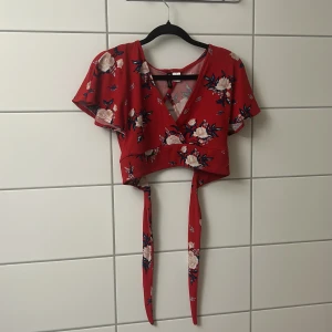 Röd blommig croppad omlottopp - Superfin röd croppad omlottopp från H&M med blommigt mönster i vitt och mörkblått. Toppen har korta ärmar, v-ringning och långa knytband i midjan. Perfekt för dig som vill ha en trendig och färgglad look.