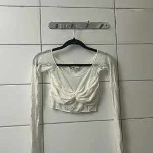 Vit croppad långärmad topp  - Superfin vit croppad topp med långa ärmar och snygg twistad detalj framtill. Tunn och lätt i materialet, perfekt för lager-på-lager eller som statement-piece. Enkel att styla med både jeans och kjol.