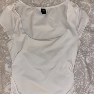 Vit topp med rynkade sidor från SHEIN - Säljer en vit topp från SHEIN med korta ärmar och rundad halsringning. Toppen har snygga rynkade detaljer längs sidorna som ger en cool och trendig look. Perfekt att styla med jeans eller kjol för en fräsch outfit.
