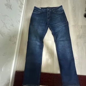 Jack and Jones  mörkblå jeans som är riktigt sköna 🤩 - Snygga Jack and jones jeans i mörkblå tvätt med klassiska fem fickor och diskreta slitningar. Jeansen har rak passform och normal midja, perfekt för en stilren och avslappnad look. Ikonisk läderpatch bak i midjan och tydliga sömmar.